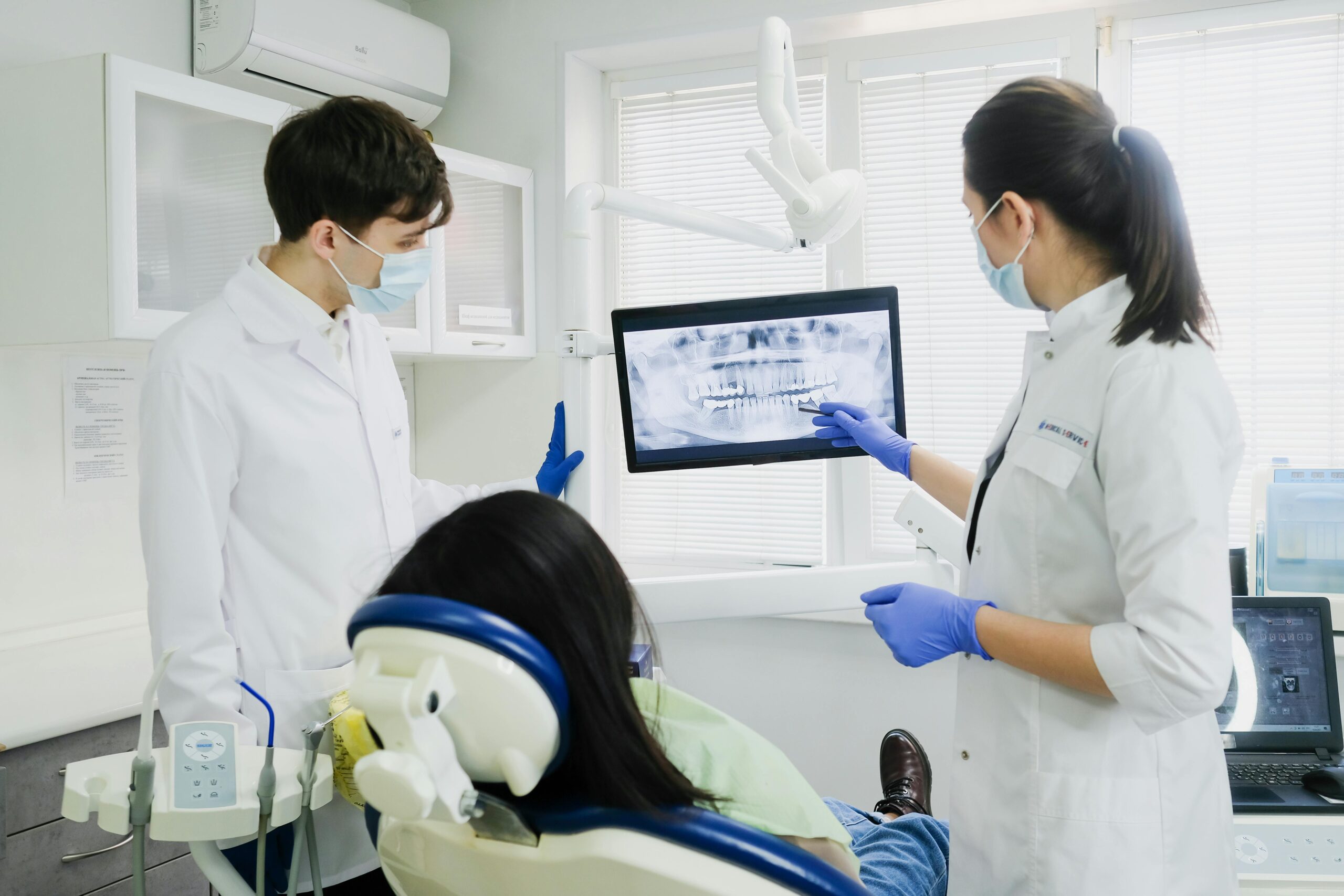 Two dentists examine a dental X-ray with a patient in a modern clinic setting.
