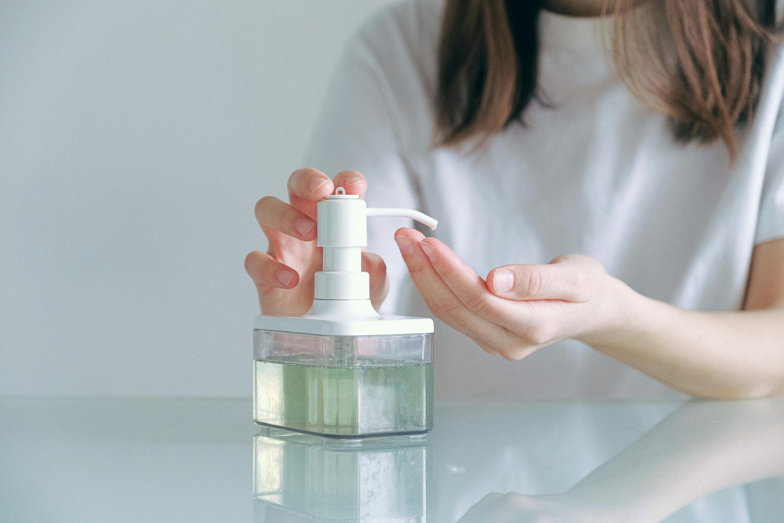 Close-up of a woman using hand sanitizer with a dispenser indoors.